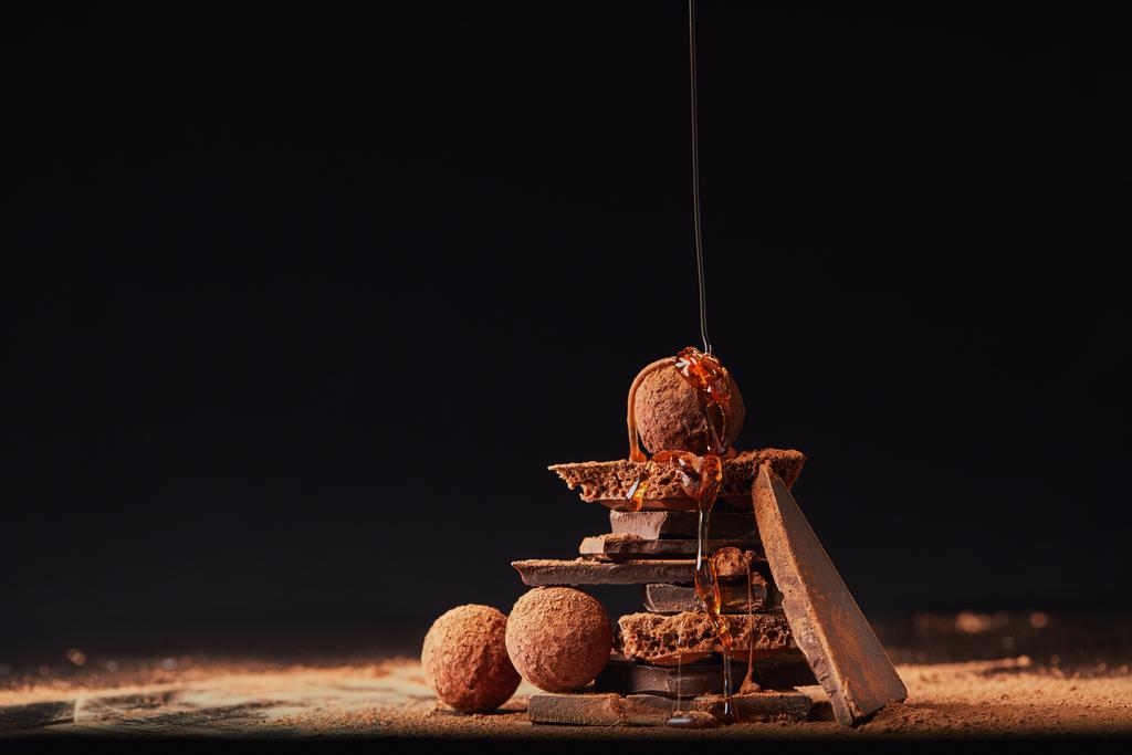 vista de perto do processo de derramamento de caramelo em trufas e barras de chocolate com cacau em pó processo em preto
 - Foto, Imagem