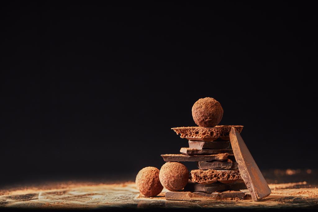 close up view of arrangement of truffles and chocolate bars with cocoa powder on black - Photo, Image