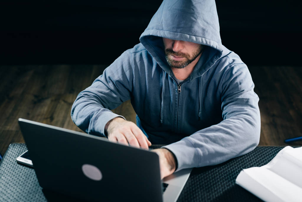 um hacker experiente trabalhando atrás de um laptop olhando atentamente para a tela
 - Foto, Imagem