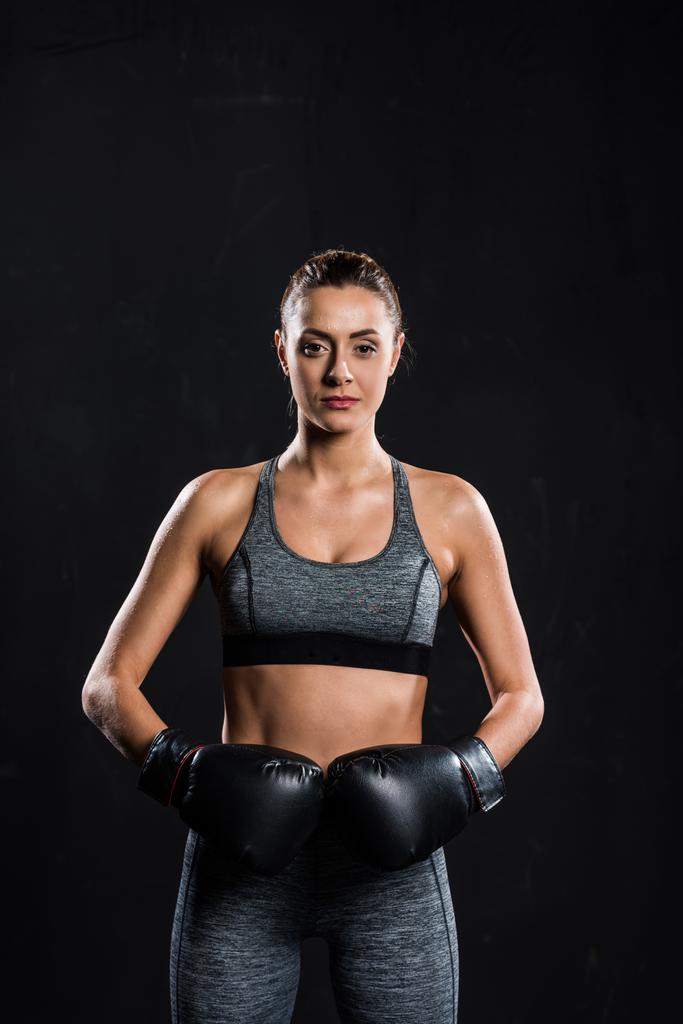 спортсменка в боксёрских перчатках, смотрящая на камеру, изолированную на черном
 - Фото, изображение