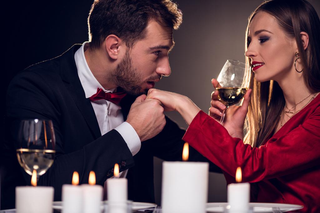 donna che beve vino mentre l'uomo le bacia la mano su appuntamento romantico nel ristorante
 - Foto, immagini