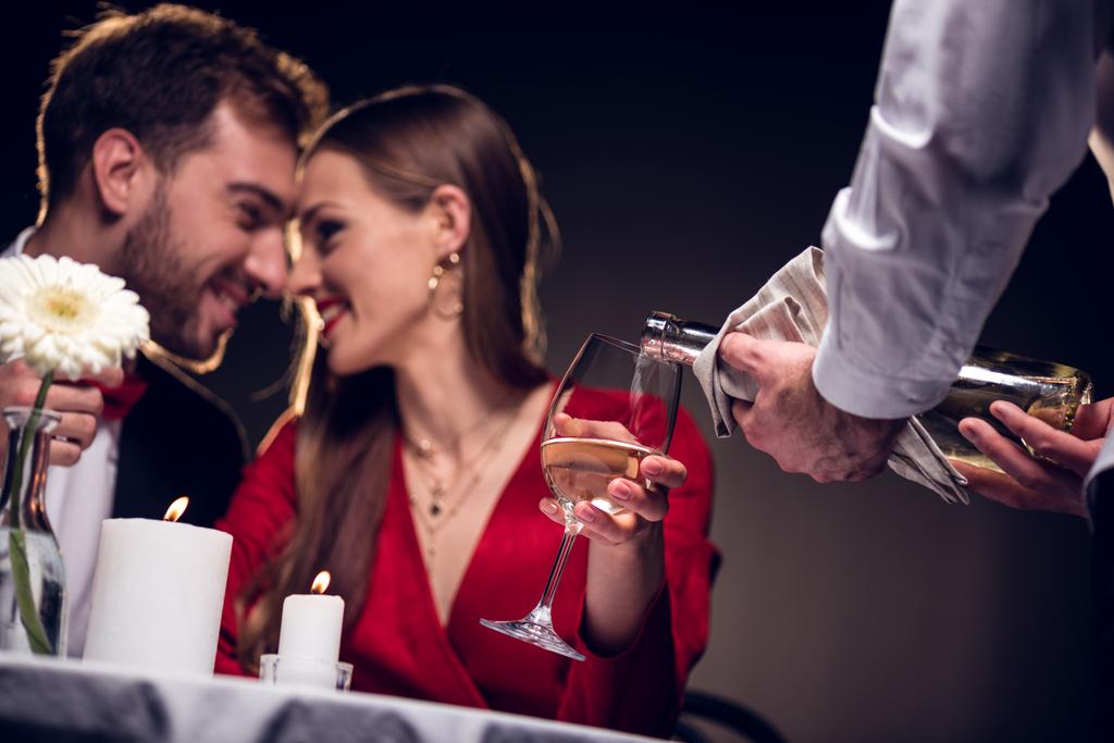 Ober gieten wijn terwijl lachende paar met romantische datum in restaurant op Valentijnsdag - Foto, afbeelding