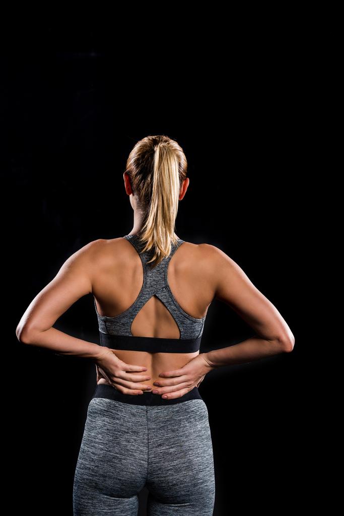 back view of athletic young woman in sportswear standing with hands on waist isolated on black - Photo, Image