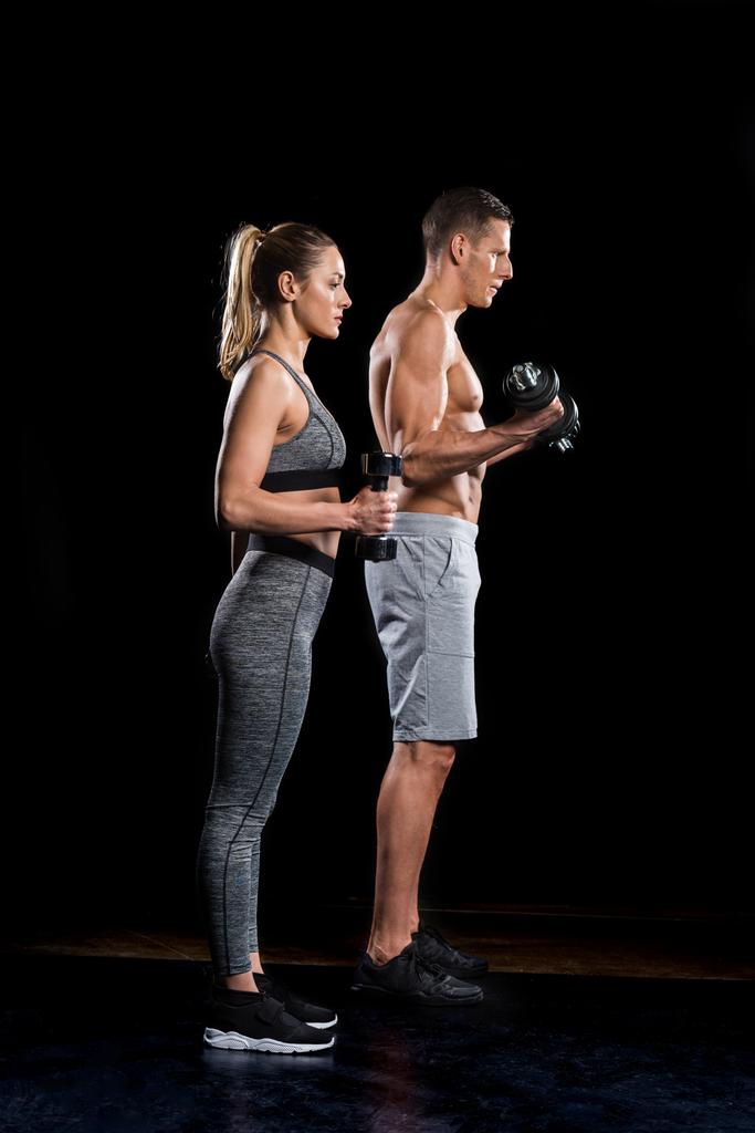 vista laterale di sporty giovane coppia esercizio con manubri su nero
 - Foto, immagini