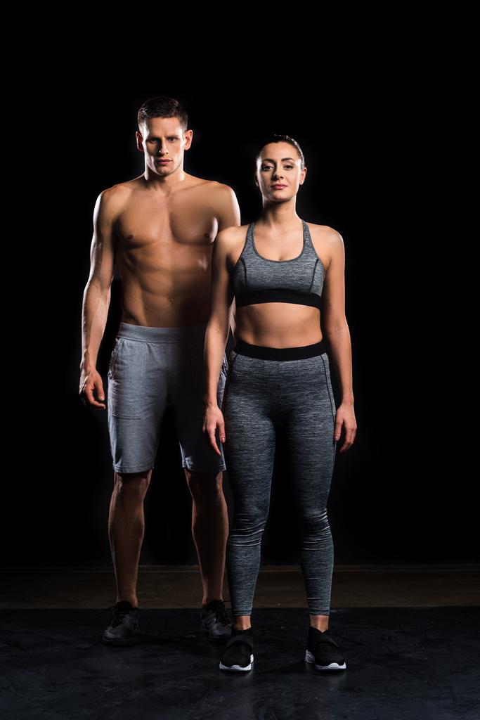 sportliches junges Paar in Sportbekleidung blickt in die Kamera auf schwarz  - Foto, Bild