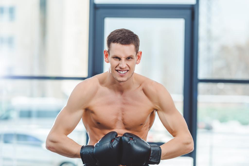 молодой без рубашки мускулистый боксер в боксёрских перчатках смотрит в камеру в спортзале
  - Фото, изображение