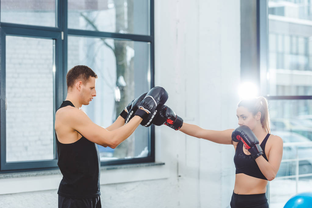 Zijaanzicht van jonge sportman en Sportvrouw boksen samen in sportschool  - Foto, afbeelding