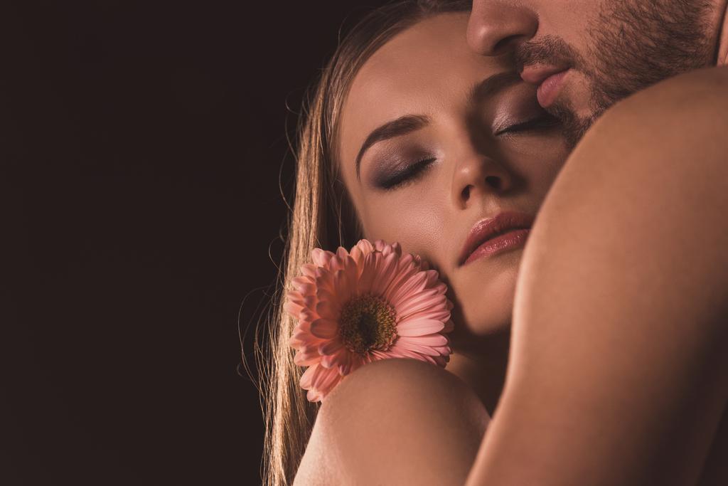 tiernos amantes con los ojos cerrados abrazando y sosteniendo la flor de gerberas, aislados en marrón
  - Foto, Imagen