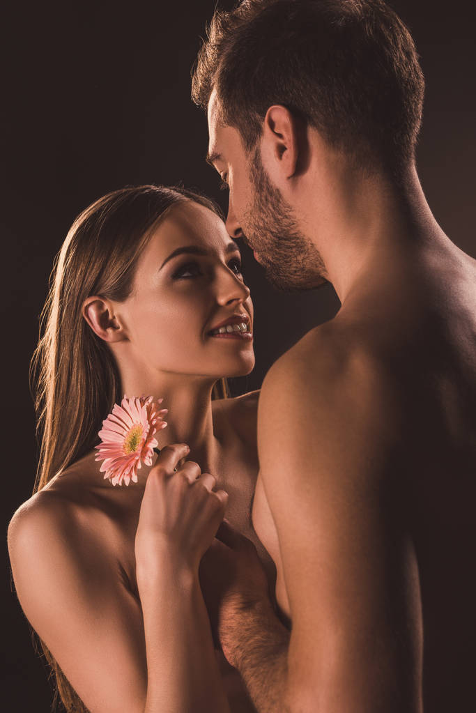 красивые влюбленные смотрят друг на друга и держат цветок герберы, изолированный на коричневом
  - Фото, изображение