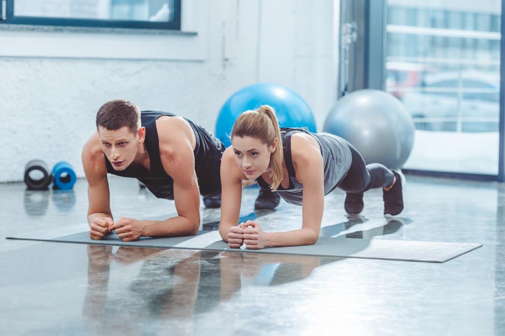 Sportliches junges Paar beim Plankentraining im Fitnessstudio  - Foto, Bild