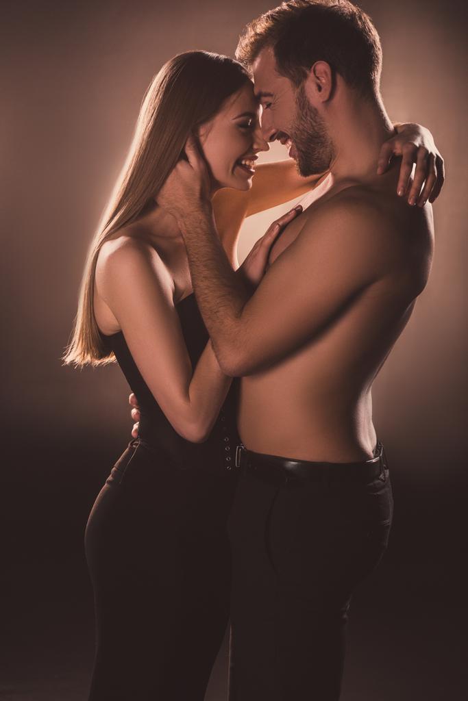 casal sensual rindo e abraçando juntos, em marrom com luz nas costas
 - Foto, Imagem
