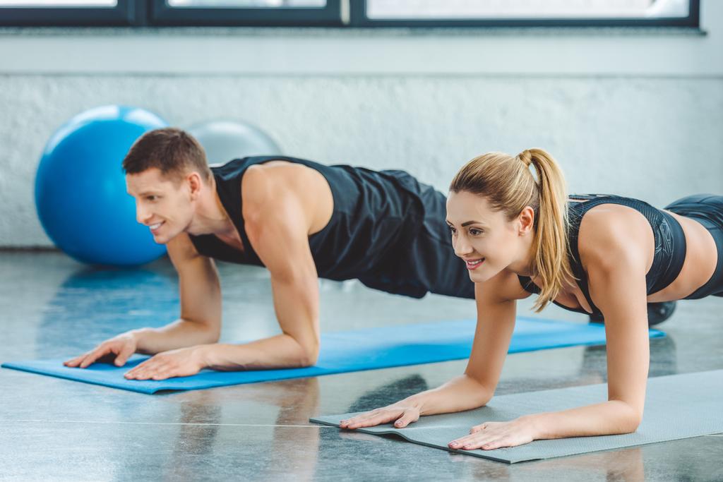 couple doing abs exercises on mats before workout in gym - Photo, Image