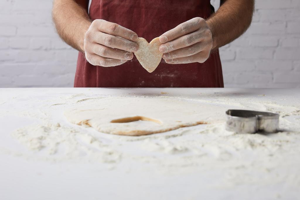 immagine ritagliata dello chef che tiene in mano un pezzo di pasta a forma di cuore, concetto di giorno di San Valentino
 - Foto, immagini