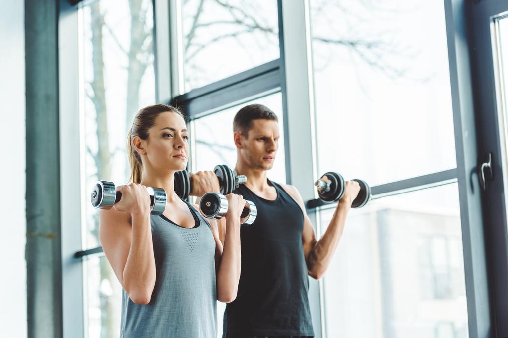 genç adam ve kadın spor salonunda dumbbells ile egzersiz odaklanmış - Fotoğraf, Görsel
