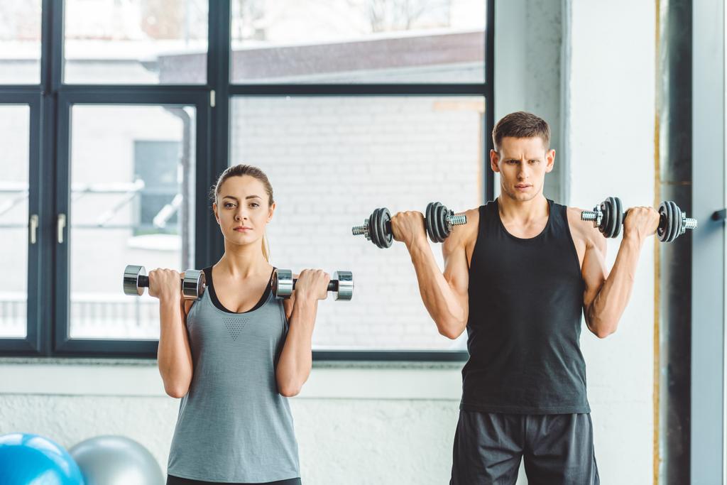 focused young man and woman exercising with dumbbells in gym - Photo, Image