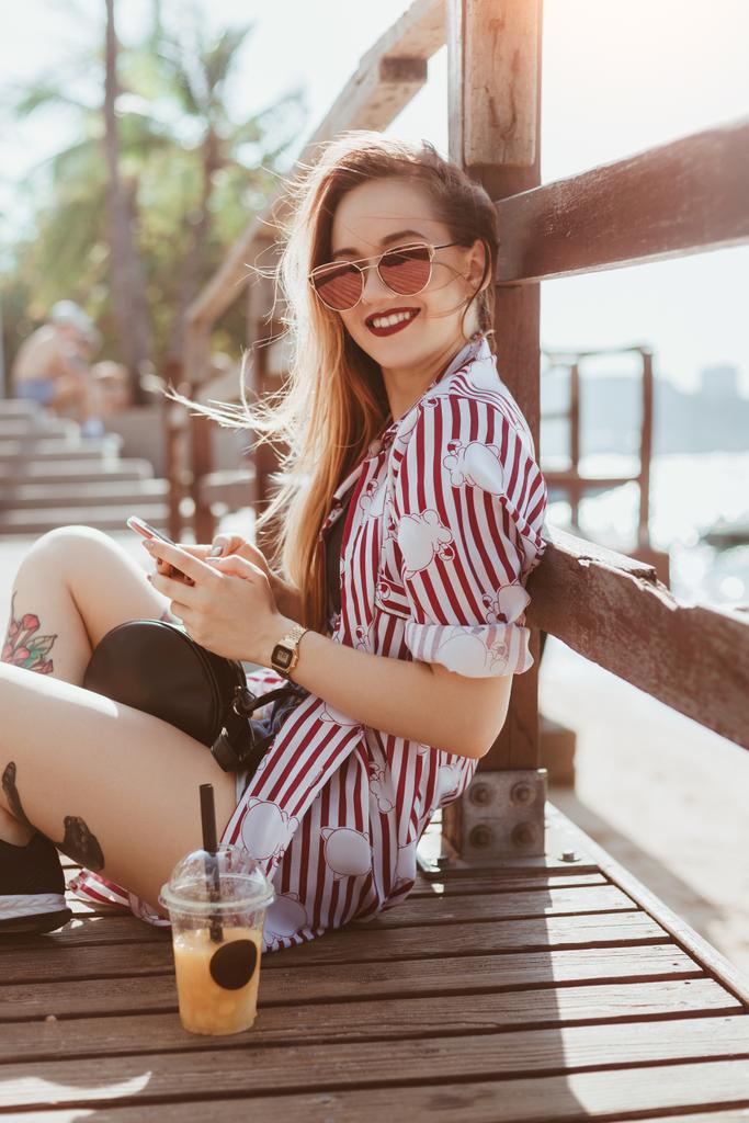 boldog fiatal nő használ smartphone ülve a mólón a beach - Fotó, kép