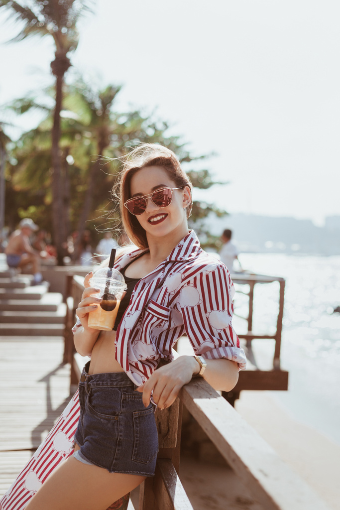hymyilevä nuori nainen muovi kuppi cocktail nojaten takaisin laiturille rannalla
 - Valokuva, kuva
