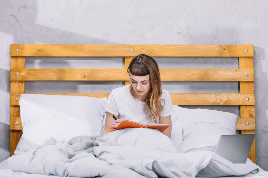 girl sitting in bed and writing something to notebook - Photo, Image