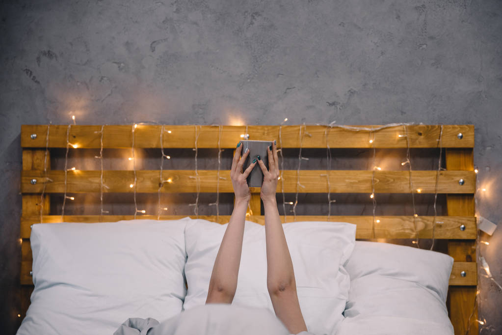 bir fincan kahve elinde tutan ve yatakta yatan kız kırpılmış görüntü - Fotoğraf, Görsel