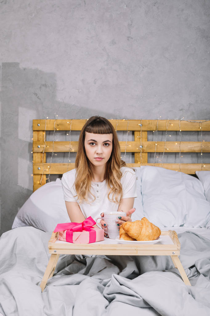 sabah kahve ve mevcut kutusu ile yatakta oturan kız - Fotoğraf, Görsel