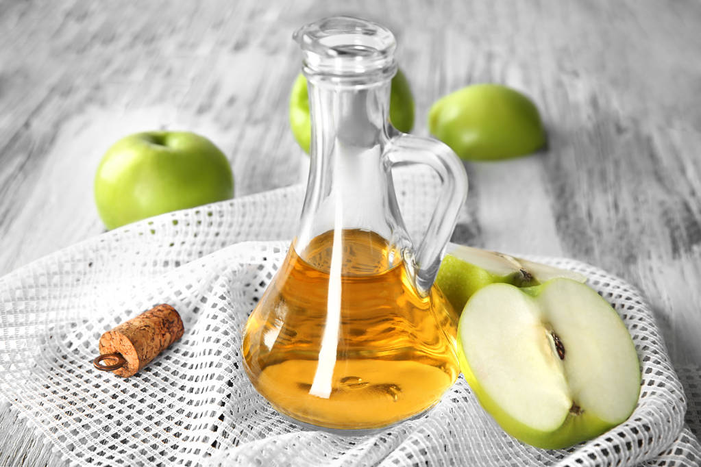 Glazen kan met appel azijn en vers fruit op tafel - Foto, afbeelding