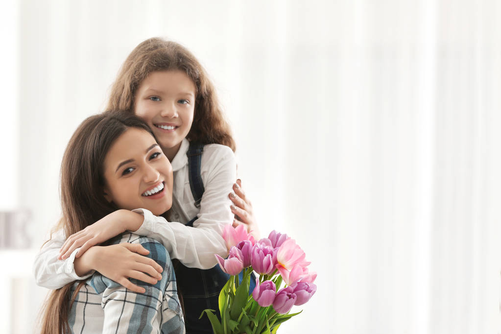 Nuori nainen ja hänen tyttärensä tulppaani kimppu sisätiloissa. Äitienpäivän juhla
 - Valokuva, kuva
