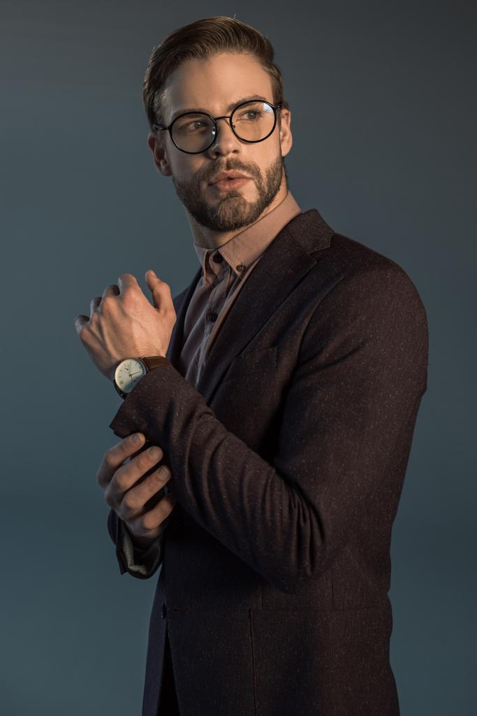 bell'uomo barbuto elegante in orologio da polso e occhiali guardando lontano isolato sul grigio
  - Foto, immagini