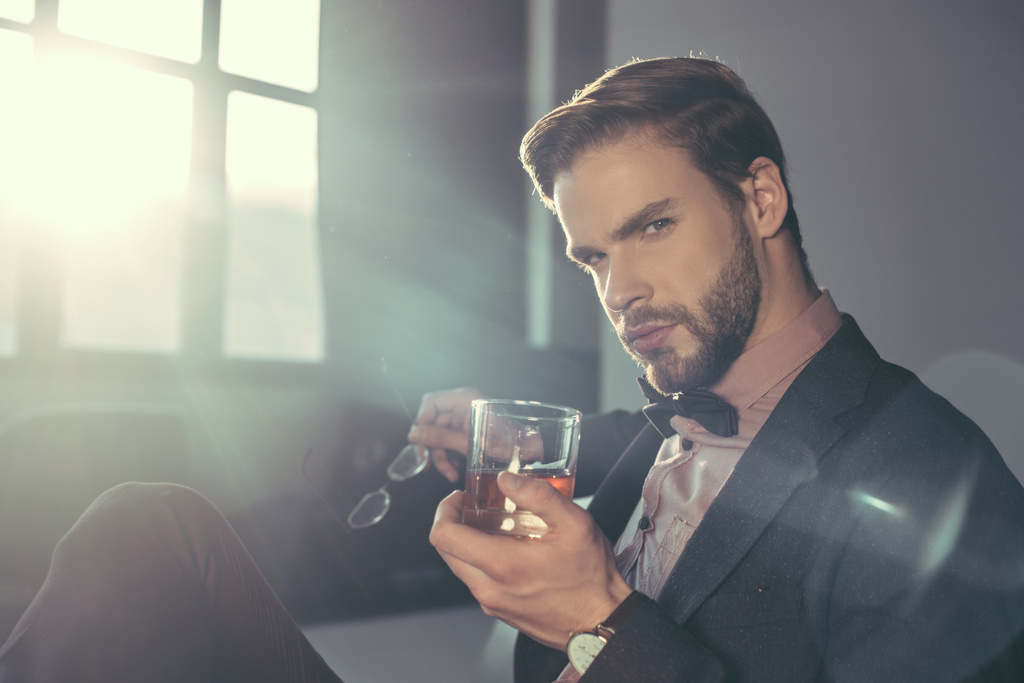 stijlvolle jonge man met bril en een glas whisky, camera kijken - Foto, afbeelding