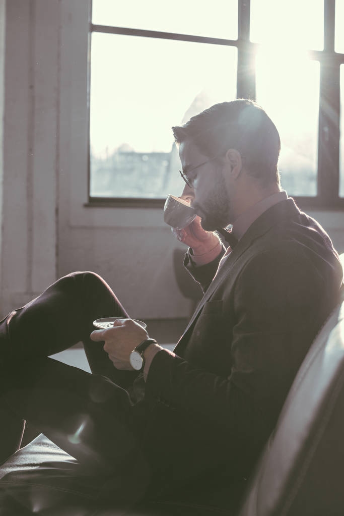 вид збоку молодого бізнесмена, який п'є каву в приміщенні
 - Фото, зображення
