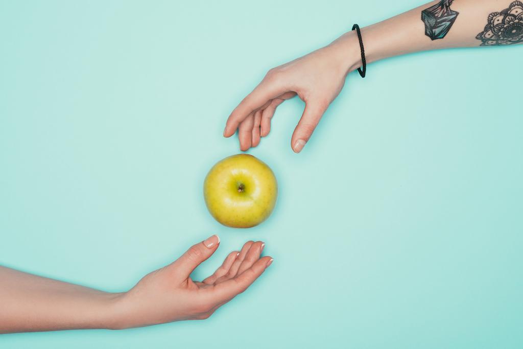 cropped shot of women passing green apple isolated on turquoise - Photo, Image
