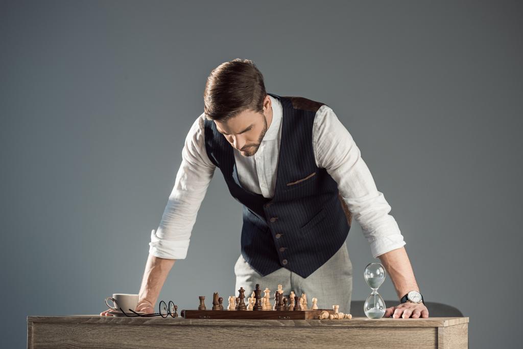 konzentrierter bärtiger, stilvoller Mann, der auf Schachbrett mit Figuren blickt - Foto, Bild