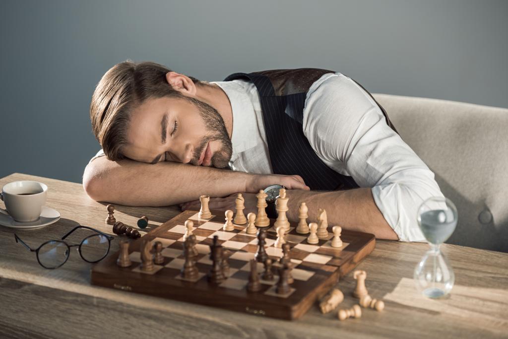 knappe jonge zakenman slapen op tafel met schaakbord - Foto, afbeelding