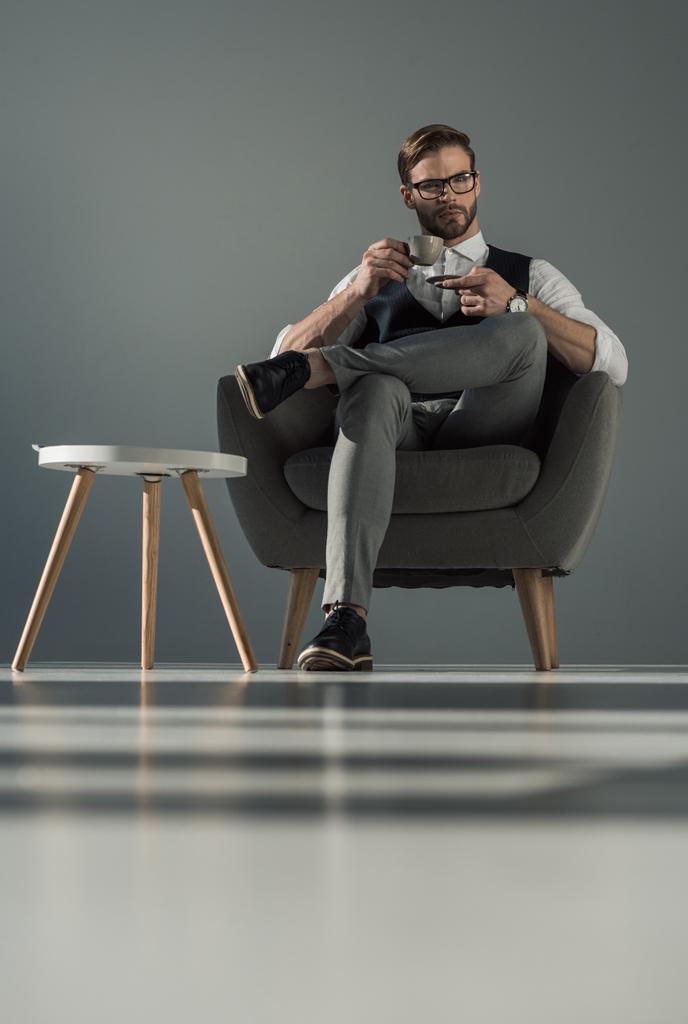 low angle view of stylish businessman with cup of coffee sitting in armchair - Photo, Image