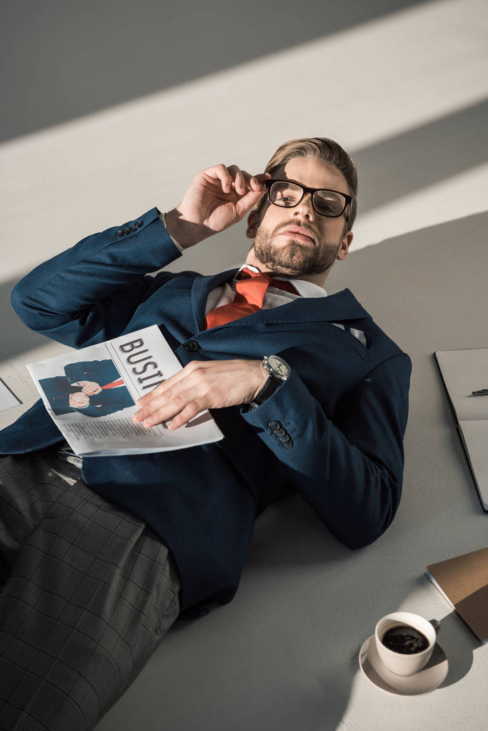 high angle view of handsome stylish young businessman with newspaper lying on floor  - Photo, Image