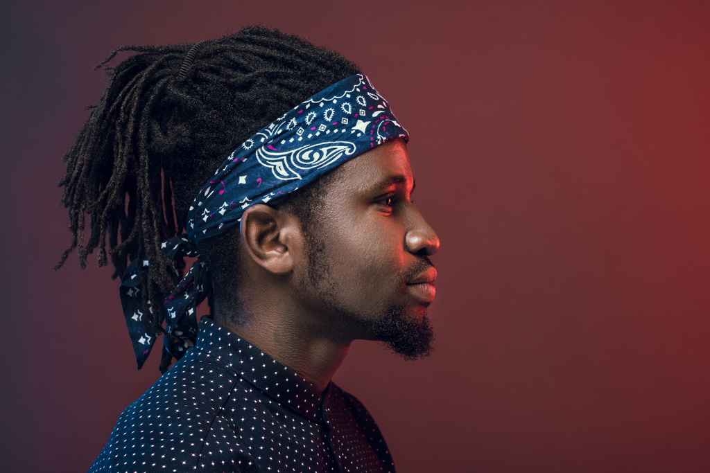 side view of handsome african american man in headband isolated on burgundy - Photo, Image
