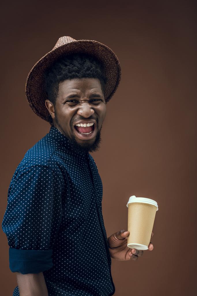 screaming african american man with disposable coffee cup isolated on brown - Photo, Image