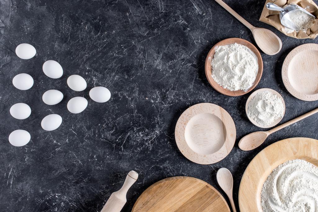 vue de dessus des oeufs crus, farine, assiettes en bois, cuillères et rouleau à pâtisserie sur la surface de marbre
 - Photo, image