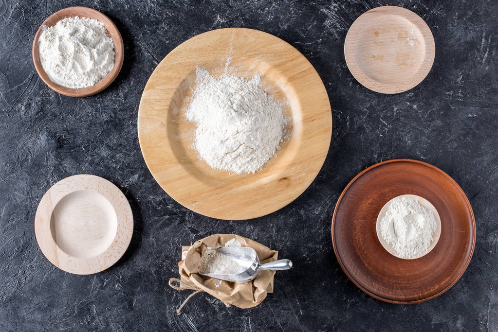 flat lay with arrangement of wooden plates and flour on dark marble tabletop - Photo, Image