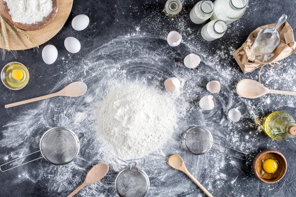 flat lay with flour and other ingredients for bakery, wooden kitchenware on dark tabletop - Photo, Image