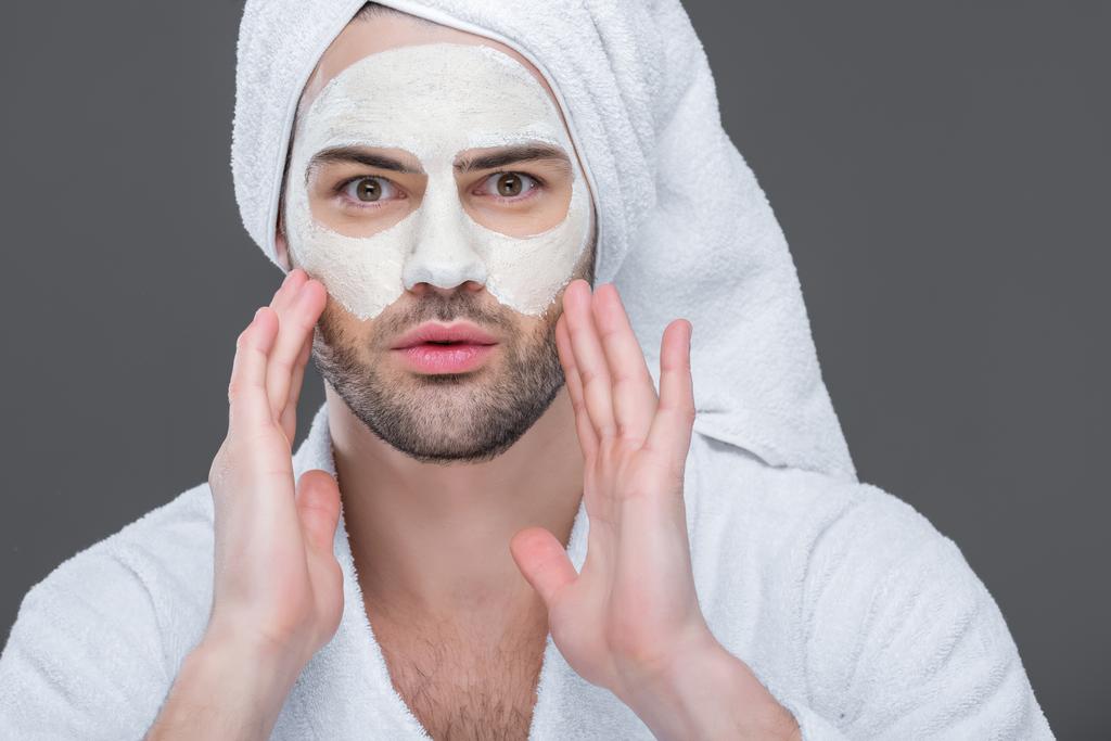 uomo barbuto in accappatoio e asciugamano con maschera di argilla sul viso, isolato su grigio, concetto di cura della pelle
 - Foto, immagini