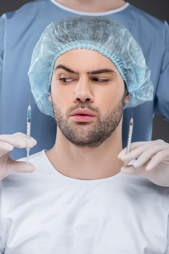 bearded handsome man in medical cap choosing beauty injections, isolated on grey - Photo, Image