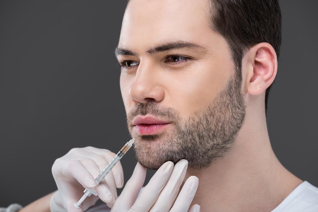 manos en guantes médicos haciendo inyección de belleza para hombre barbudo, aislado en gris
 - Foto, imagen