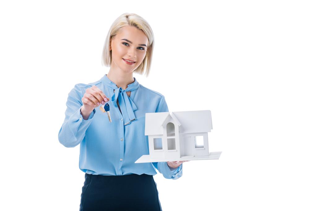 piękny realtor uśmiechający się trzymając klucz i dom model na białym tle - Zdjęcie, obraz