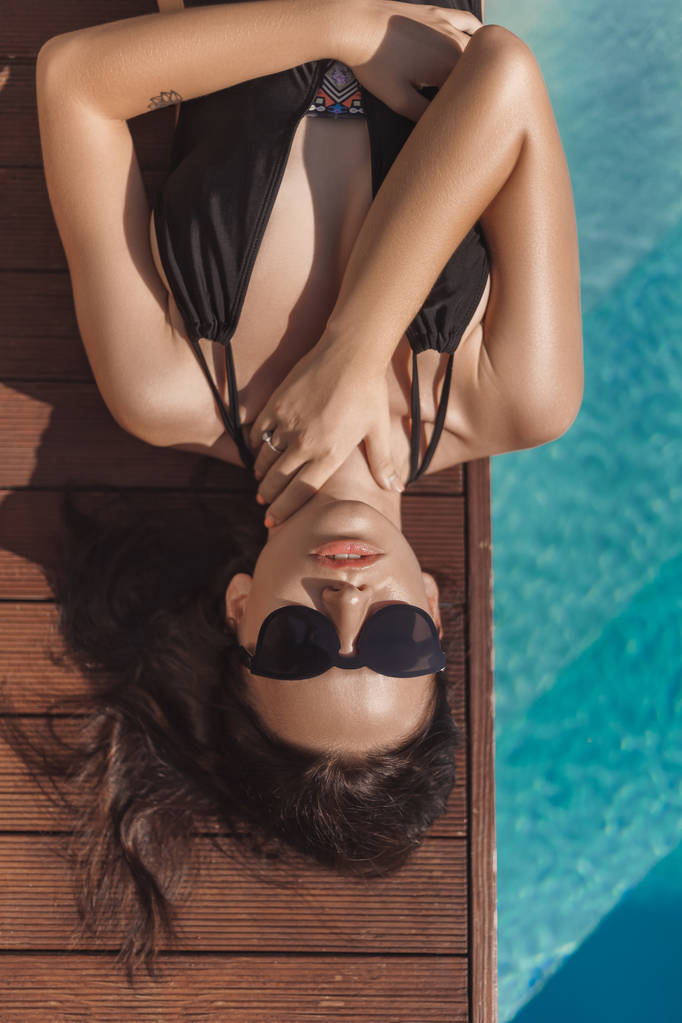 top view of attractive young woman in black swimsuit lying at poolside - Photo, Image
