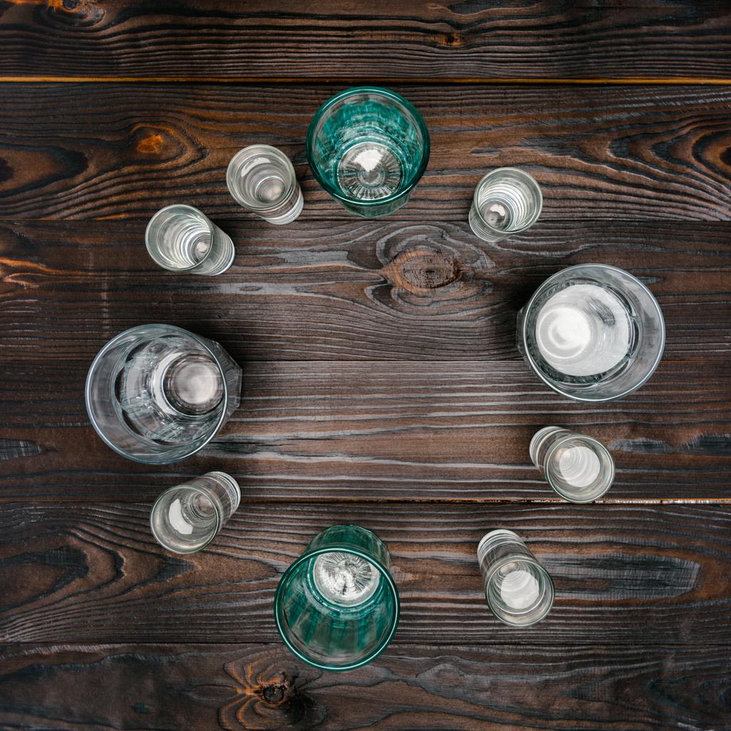 vista superior do círculo com óculos de diferentes tamanhos com água na mesa de madeira
 - Foto, Imagem