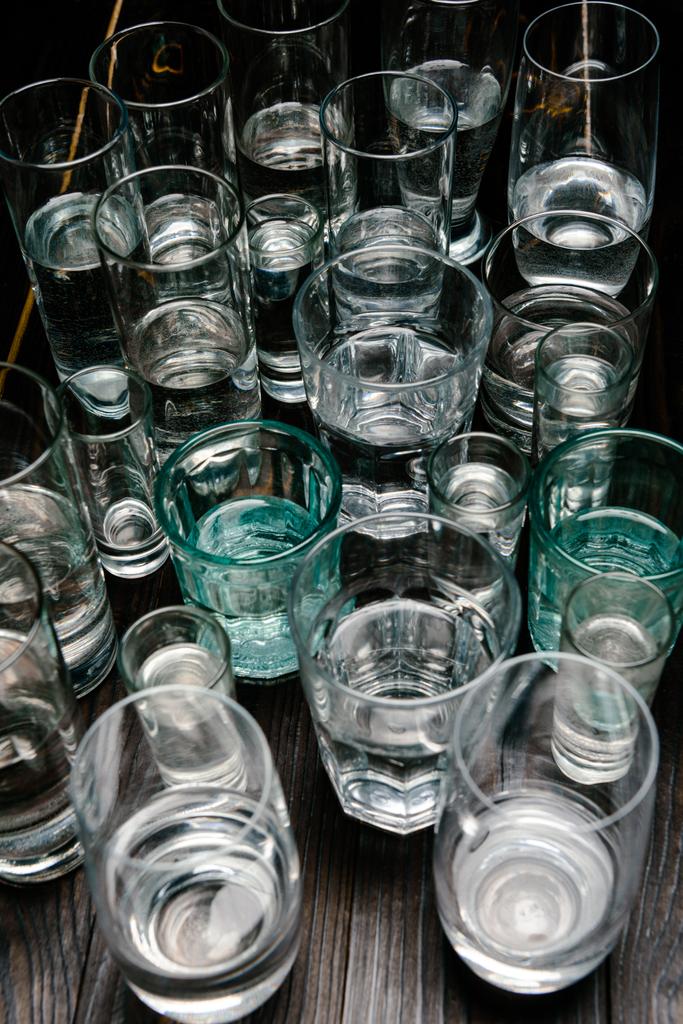 high angle view of different sized glasses with water on wooden table - Photo, Image