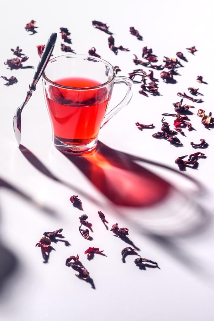 glass cup of hibiscus tea with spoon and scattered tea on table - Photo, Image