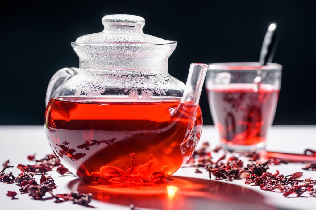 bule de vidro com chá de hibisco e xícara com colher na mesa
 - Foto, Imagem