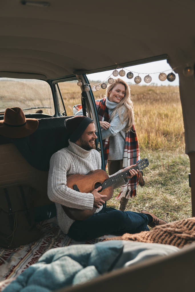 Knappe jongeman gitaarspelen terwijl vrouw luisteren een lied in de buurt van auto - Foto, afbeelding