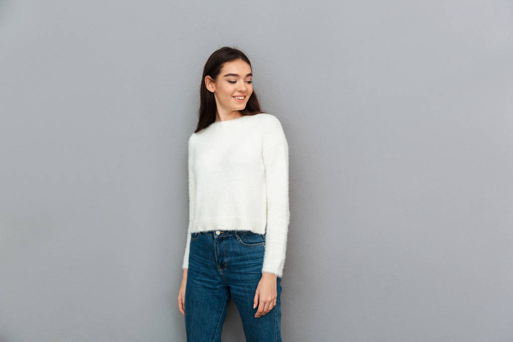 Jonge mooie brunette vrouw in de witte trui en jeans lookin - Foto, afbeelding